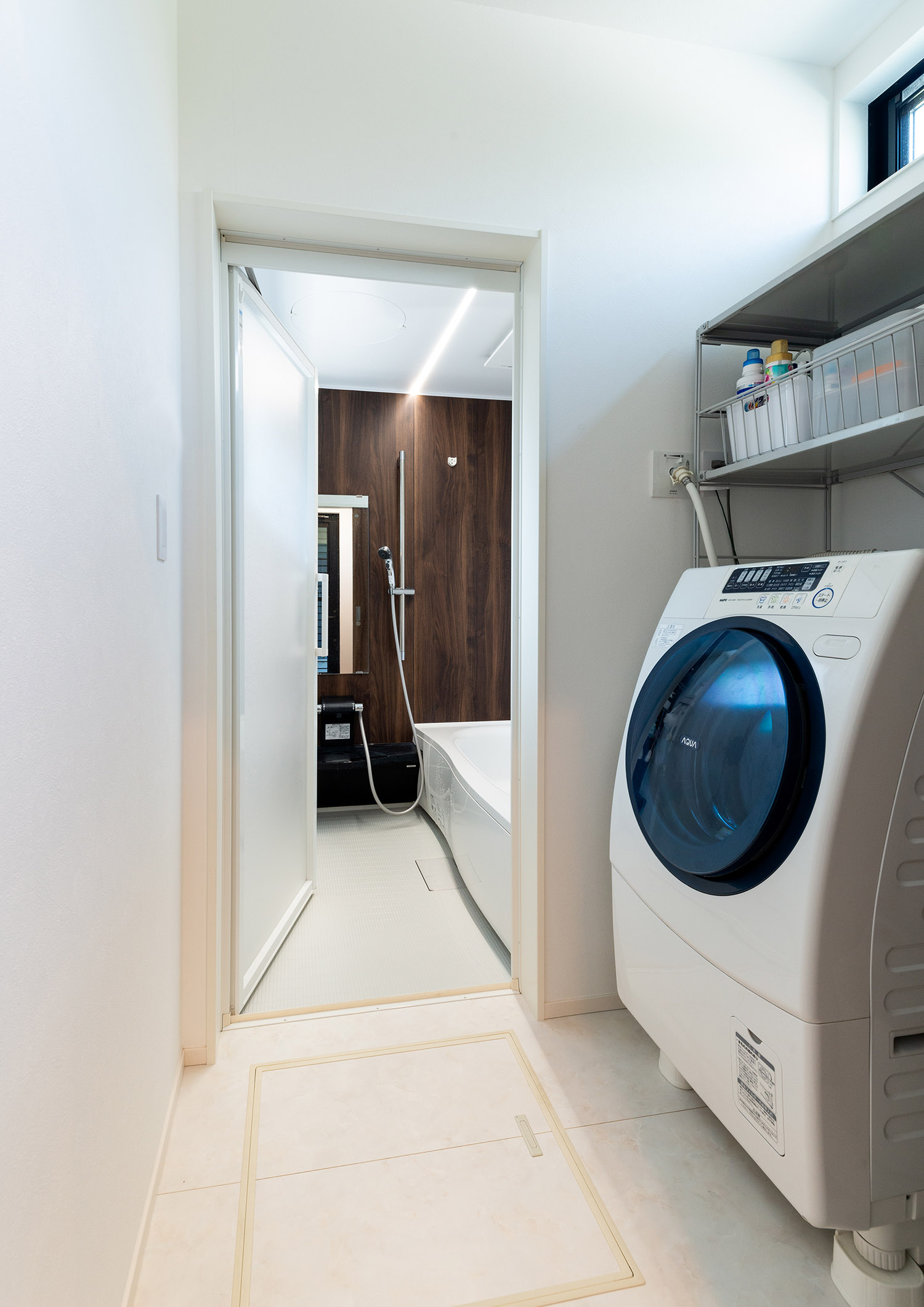 洗濯機を置いた脱衣所の奥にある、木目の壁がアクセントになった浴室・デザイン住宅 注文住宅・デザイン住宅建築実例_『CASE763 ソト黒ウチ白』_浴室・洗面所