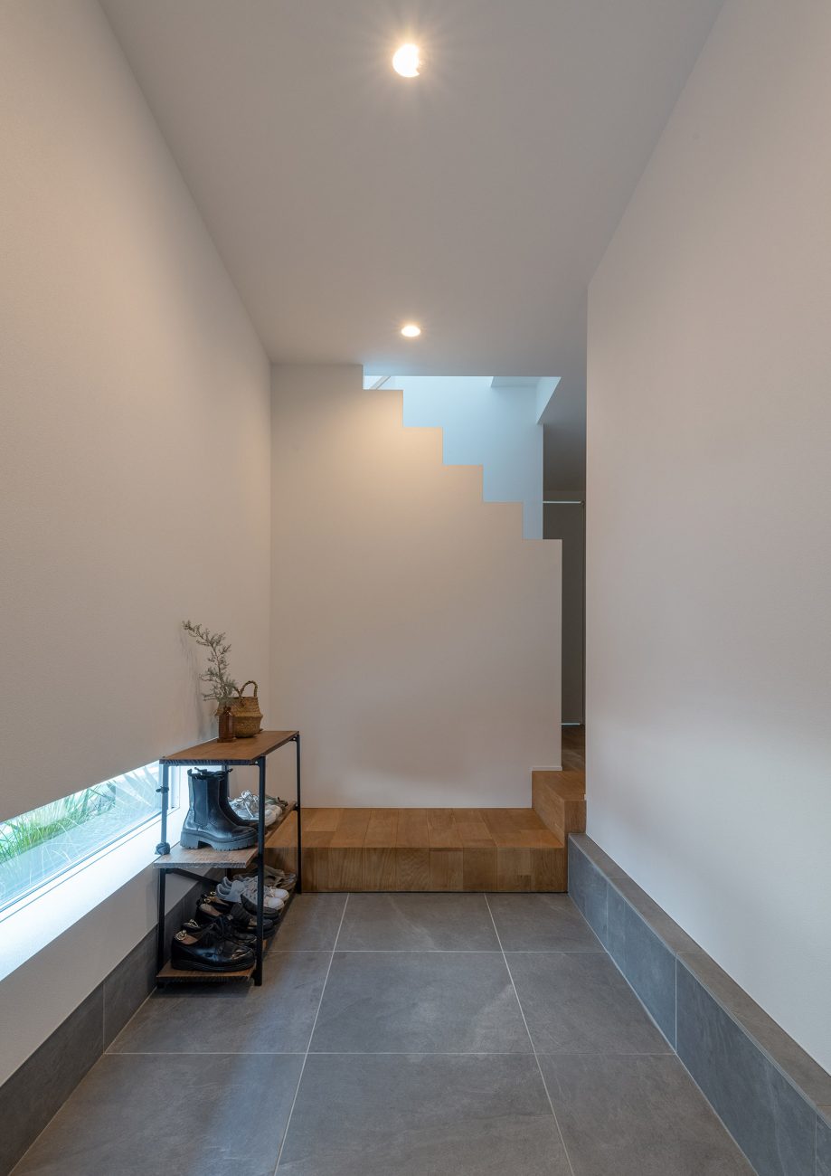 地窓がある白い壁に囲まれたタイル床の玄関・デザイン住宅 注文住宅・デザイン住宅建築実例_『CASE770 籠(こ)もれる家』_玄関