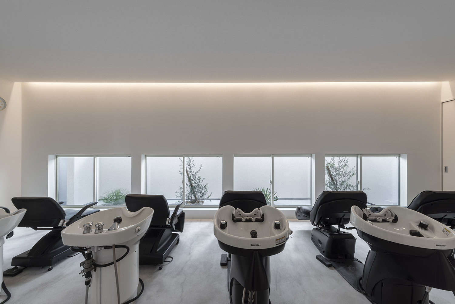 壁際に間接照明が取り付けられたシャンプー台が並んだヘアサロンの店内・店舗併用住宅 注文住宅・デザイン住宅建築実例_『CASE773 hairsalon Laetitia loco』_店舗