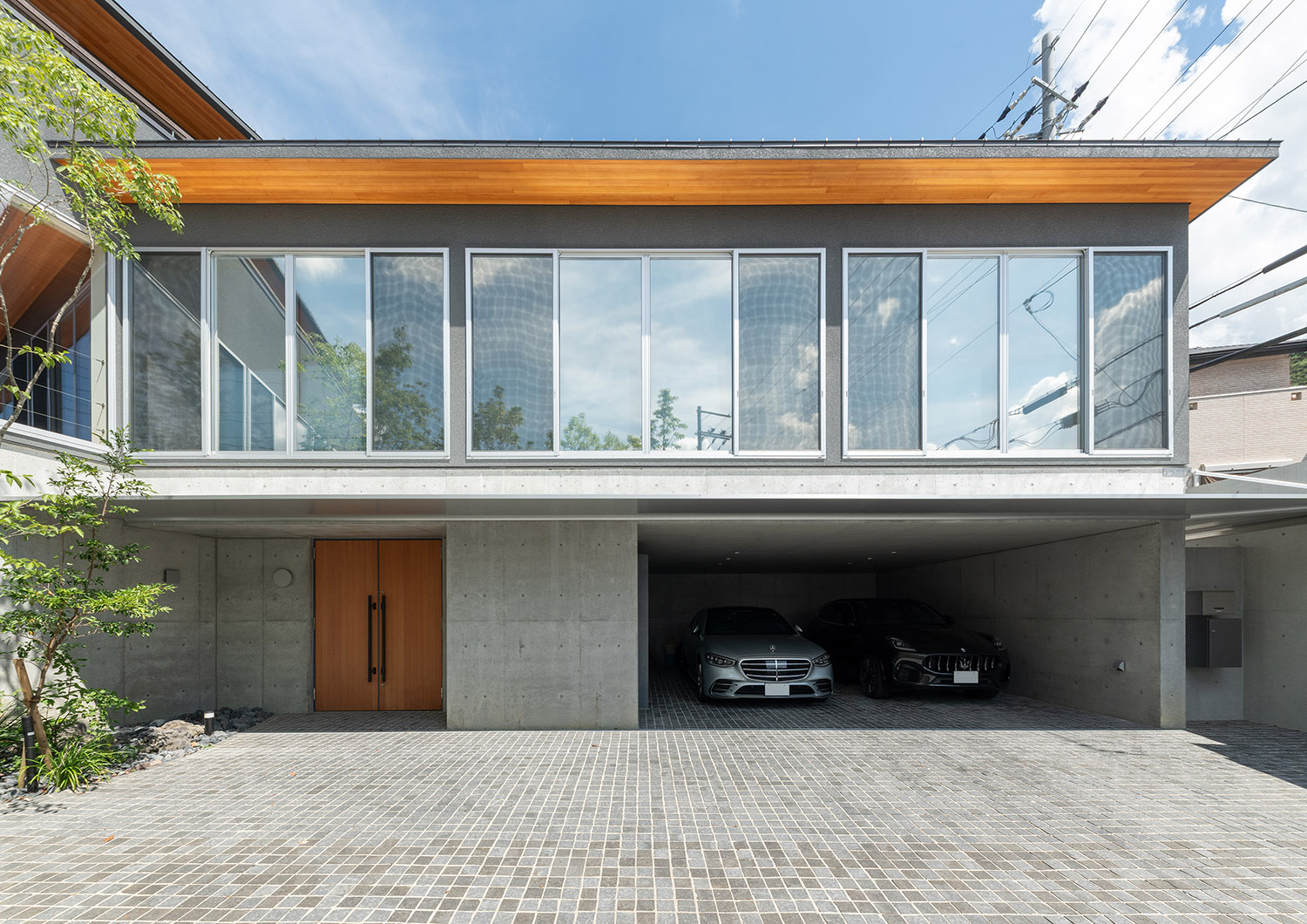 コンクリートの外壁に木製の軒天が印象的な二階建ての家の外観